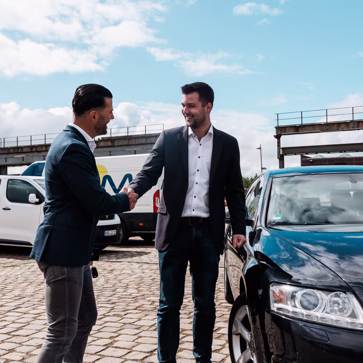 Händler und Gökhan beim Handschlag vor einem Fahrzeug